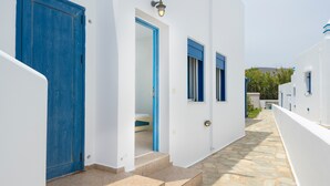 A narrow pathway leading to a building with a blue door and windows, stone flooring, and a clear sky.