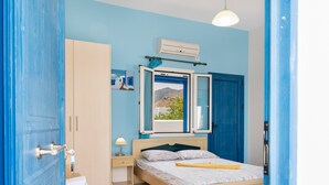 A bedroom with a bed, a nightstand, a window with curtains, a wardrobe, and an air conditioning unit.