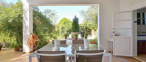 An outdoor patio with a table and chairs, surrounded by potted plants and a view of the garden.