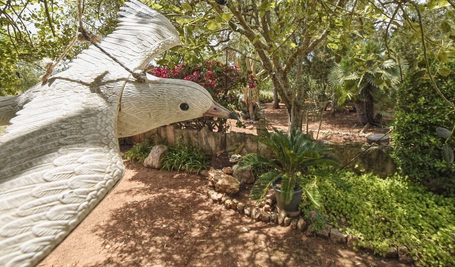 A bird sculpture in a garden with trees and plants.