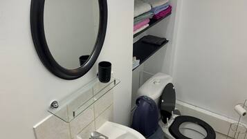 A bathroom with a white sink, a black toilet, a mirror, and a shelf with folded towels.