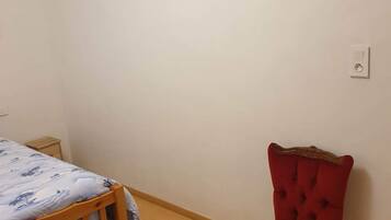 Een slaapkamer met een houten bed, een rode fauteuil, een nachtkastje en een stopcontact.