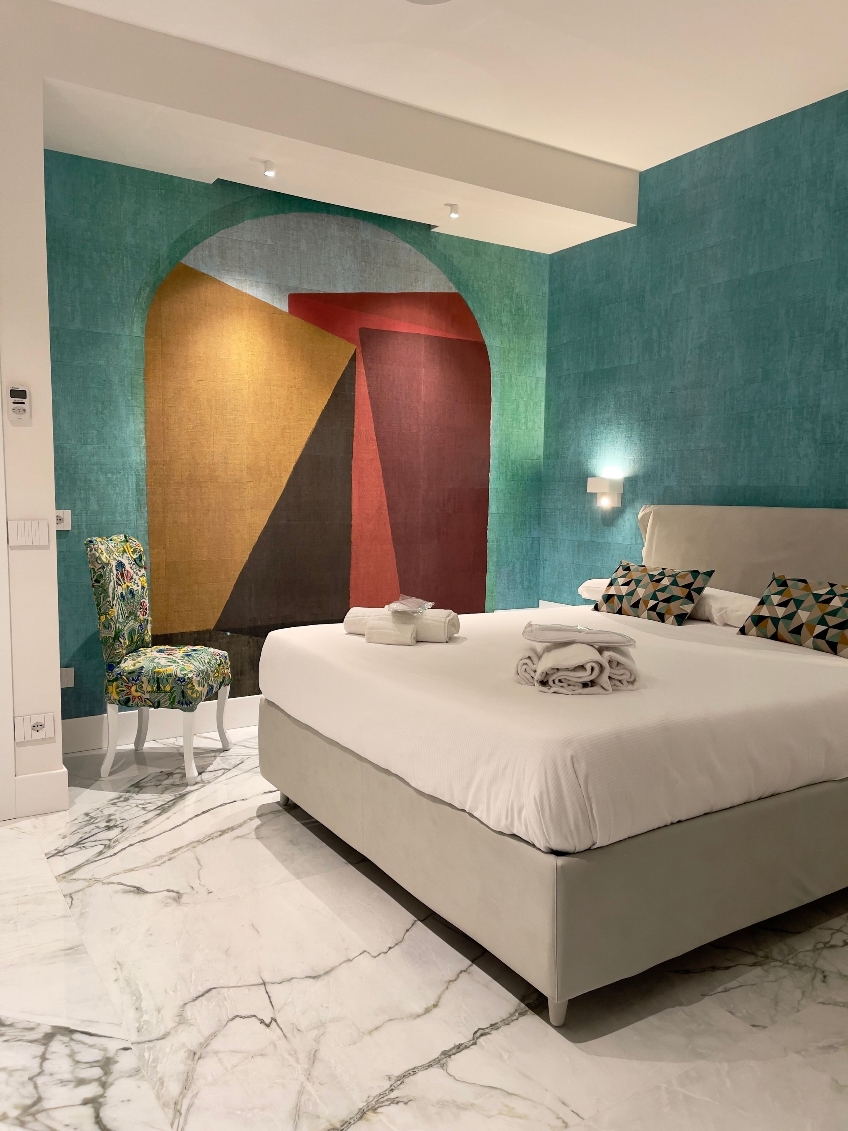 Quarto de hotel moderno com uma cama grande, uma cadeira e um design de parede exclusivo.