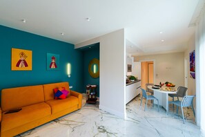 Un salon moderne avec un canapé, un coin repas avec des chaises, une cuisine et des œuvres d’art accrochées aux murs.