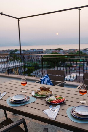 A dining table set with plates, cutlery, and glasses, overlooking a cityscape with a body of water. - Apartment 'Gio Mar Blu' with Sea View, Wi-Fi and Air Conditioning (Piano di Sorrento)