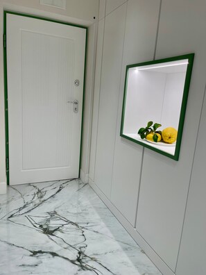 Un pasillo con una puerta blanca, piso de mármol y un espejo con marco verde fijado a la pared.