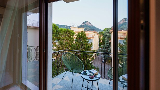 A balcony with a view of buildings and mountains, a chair, and a table with a book and a cup. - Apartment 'Gio Mar Green' with Mountain View, Wi-Fi and Air Conditioning (Piano di Sorrento)