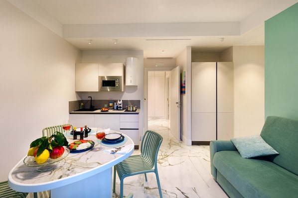 A modern kitchen with a dining area, a green sofa, and a marble floor.