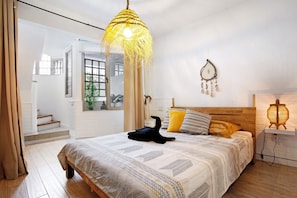 Ein Schlafzimmer mit Bett, einer Pendelleuchte, einer Wanddekoration und einem Nachttisch mit Lampe.