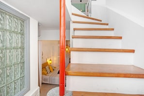 Eine Treppe mit Holzsitzen und einer roten Säule, die zu einem Zimmer mit einem Bett und einer Lampe führt.