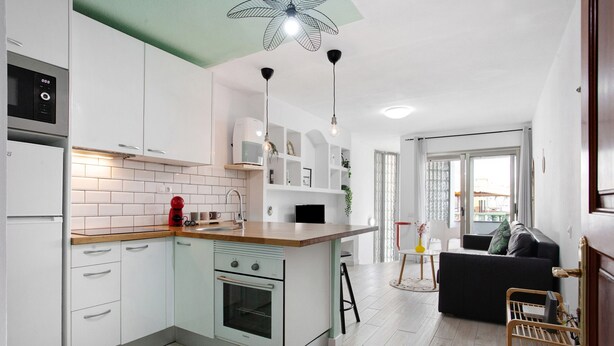 Una cocina moderna con armarios blancos, encimera de madera y horno empotrado.