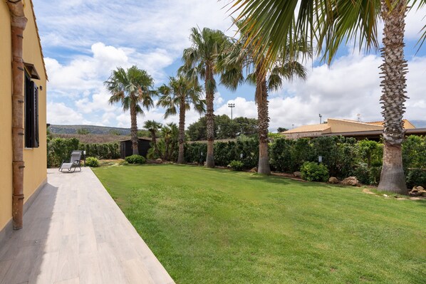 A courtyard with palm trees, a lawn, and a building with a tiled roof.