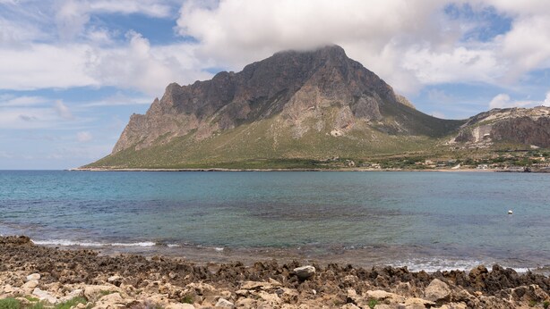 Una costa rocosa con una montaña imponente al fondo.