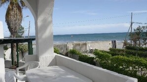 A balcony with a view of the sea, a white building, and some greenery.
