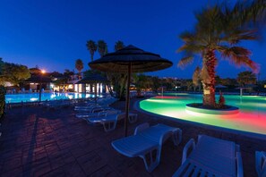 Un área de piscina con sillones de descanso, una palmera y un pabellón.