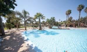 Una piscina con sillas de descanso y palmeras, rodeada de edificios.
