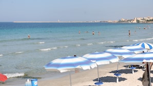 Ein Strand mit Sonnenschirmen und Menschen im Wasser.
