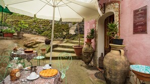 Un patio al aire libre con una mesa lista para comer, rodeado de macetas con plantas y un muro de piedra rústica.