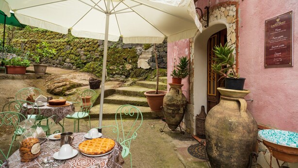 Un patio al aire libre con una mesa lista para comer, rodeado de macetas con plantas y un muro de piedra rústica.