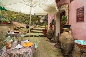 An outdoor patio with a table set for dining, surrounded by potted plants and a rustic stone wall.