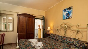 Un dormitorio con cama, armario de madera, una silla, lámpara y un cuadro en la pared.