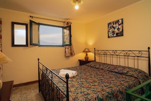 A bedroom with a bed, a window, a painting, and a lamp.
