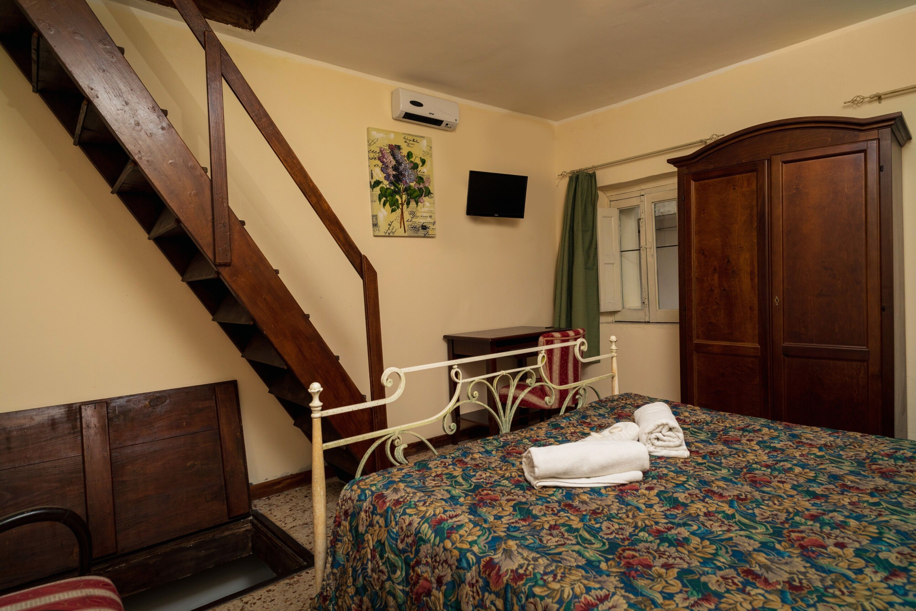 Een slaapkamer met een houten trap, een bed met een bloemenprint sprei, een houten garderobe en een flatscreen televisie aan de muur.