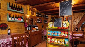 Un interior rústico con paredes de madera, estantes llenos de botellas de vino, un menú en una pizarra y bolsas de aperitivos.