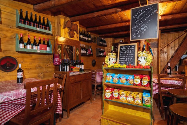 A rustic interior with wooden walls, shelves of wine bottles, a chalkboard menu, and snack bags.
