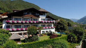 Un hôtel à plusieurs étages, doté de balcons ornés de fleurs, d’une piscine et surplombant un paysage montagneux.