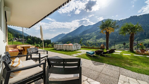 An outdoor patio with a view of mountains, a table with chairs, and a lounge chair. - Apartment "Haus Reimon Monika" with Mountain View & Wi-Fi (St.Leonhard in Passeier)