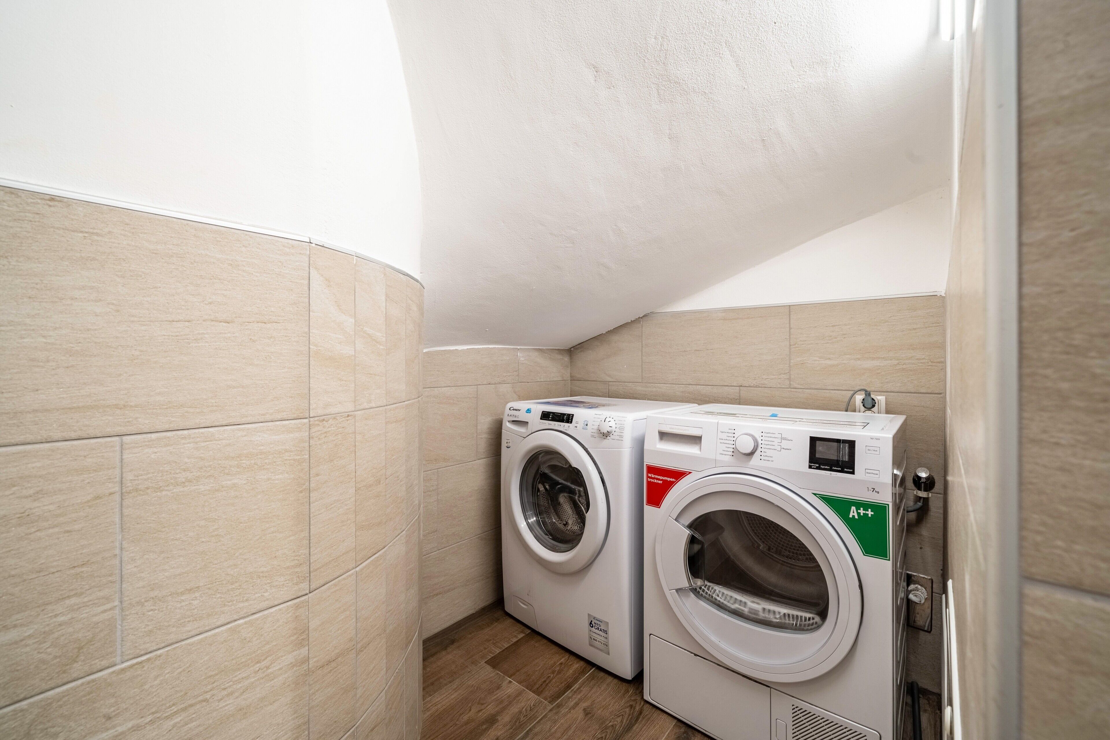 Ein Waschraum mit zwei Frontlader-Waschmaschinen, beige gefliesten W änden und Holzboden.