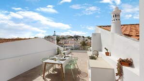 Eine Dachterrasse mit einem Esstisch, einer weißen Wand und Blick auf die Stadtlandschaft.