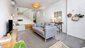 Ein modernes Wohnzimmer mit einer Couch, einem Couchtisch, einem Fernseher und einer Treppe, die in eine obere Etage führt.