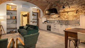 Une cuisine moderne avec un mur en pierre, des étagères intégrées et un coin repas agrémenté d’un canapé et de chaises verts.