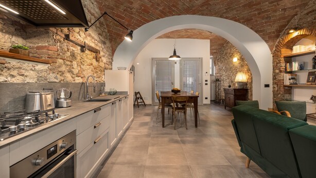 Une cuisine avec un mur en briques, des appareils modernes et une porte en arc donnant sur un coin repas.