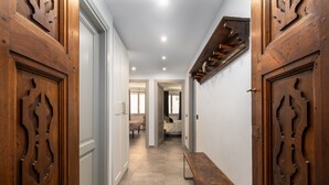 Un couloir avec des portes en bois, un banc et, au loin, un lit.