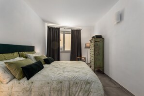 Une chambre à coucher avec un lit, des rideaux, une commode et une lampe.