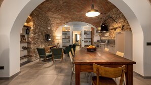 Un espace repas doté d’un plafond en briques, d’une table et de chaises en bois, qui donne sur une cuisine équipée d’un réfrigérateur et d’étagères.