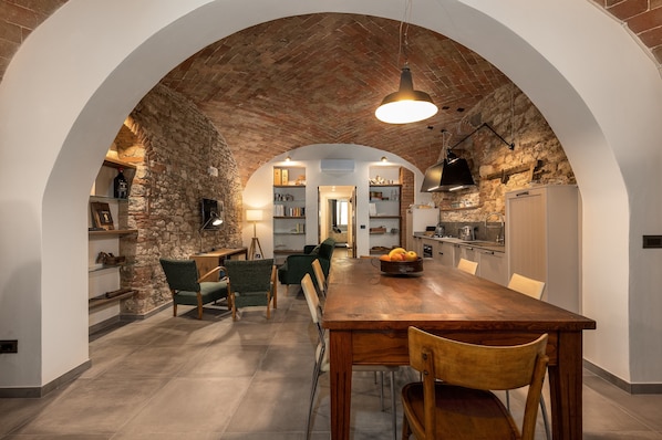 Un espace repas doté d’un plafond en briques, d’une table et de chaises en bois, qui donne sur une cuisine équipée d’un réfrigérateur et d’étagères.