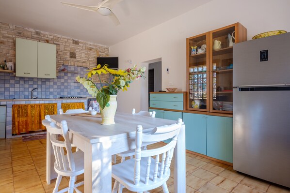 Una cocina con una mesa de comedor, sillas, un refrigerador, armarios y un televisor.