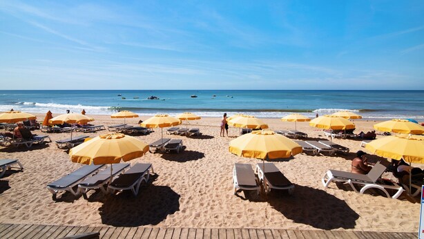 Une plage avec des transats et des parasols jaunes, une terrasse en bois et l’océan en arrière-plan.