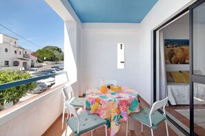 Un balcón con una mesa preparada para dos, una silla y vistas a coches estacionados y edificios.
