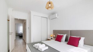 Et hotelværelse med seng, et natbord, en lampe og en aircondition.