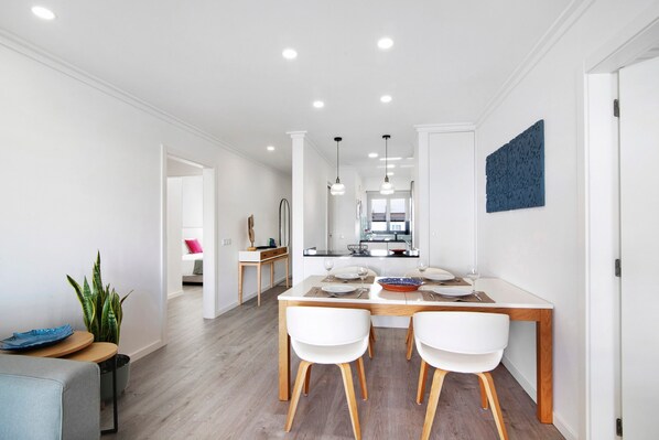 A modern dining area with a white table, two white chairs, and a wooden floor.