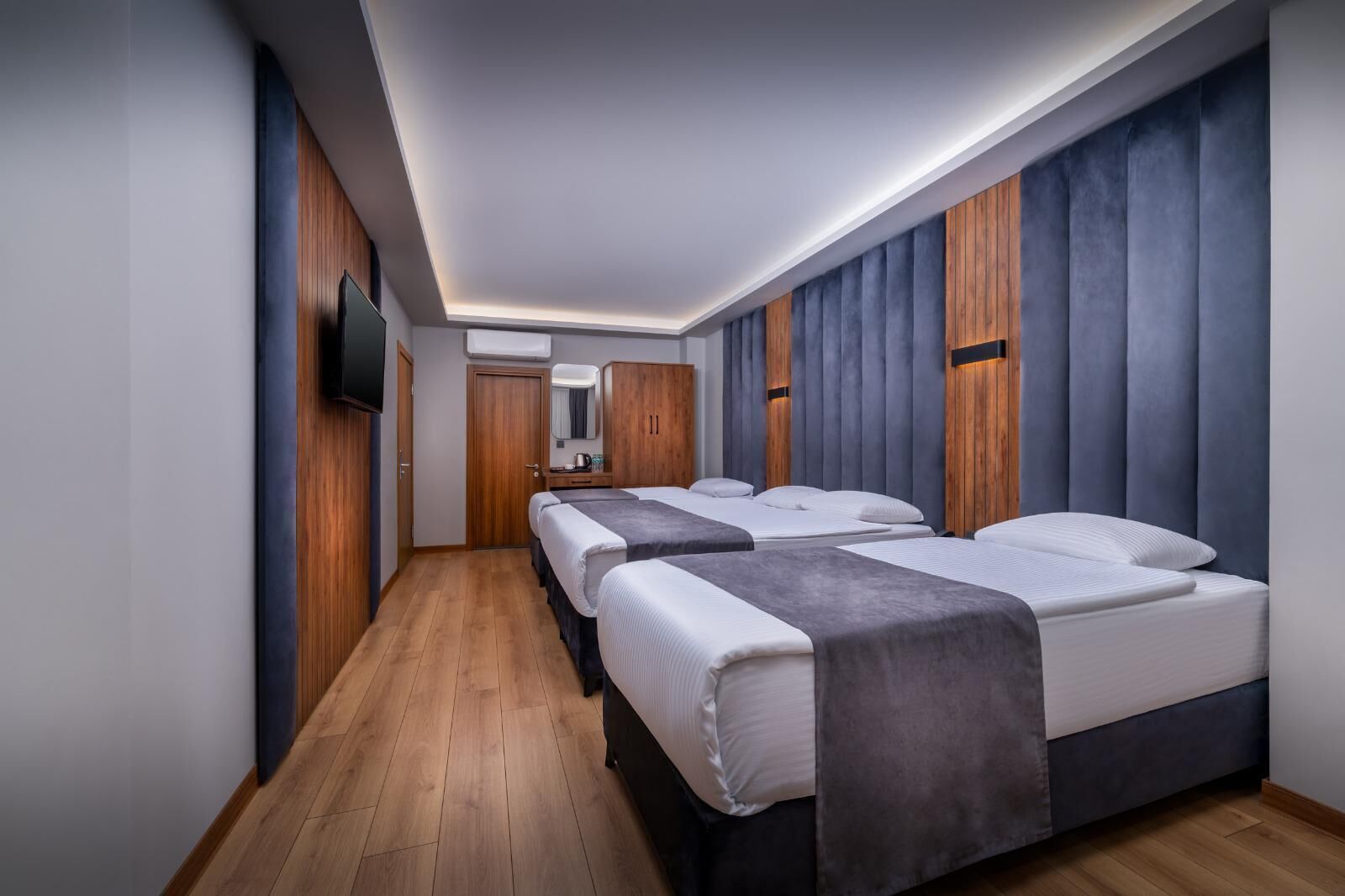 Una habitación de hotel moderna con dos camas, suelo de madera, televisor de pantalla plana y un ventanal grande.