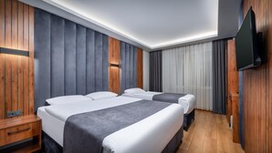 Een moderne hotelkamer met een groot bed, twee kleinere bedden, houten lambrisering, een flatscreen televisie en een houten vloer.