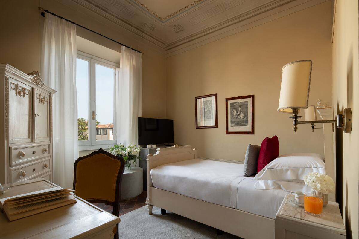 Une chambre d’hôtel comprenant un lit, un bureau avec une chaise, une télévision, une lampe et une fenêtre avec des rideaux.