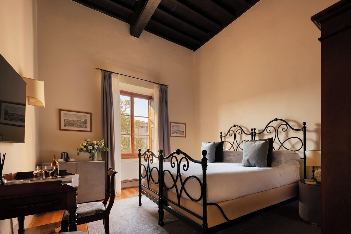A bedroom with a bed, a desk, a chair, a window with curtains, and a framed picture on the wall.