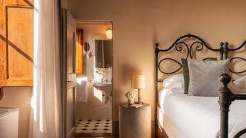 Une chambre à coucher avec un lit, une petite table ronde avec une lampe, un miroir et une vue sur la salle de bain.